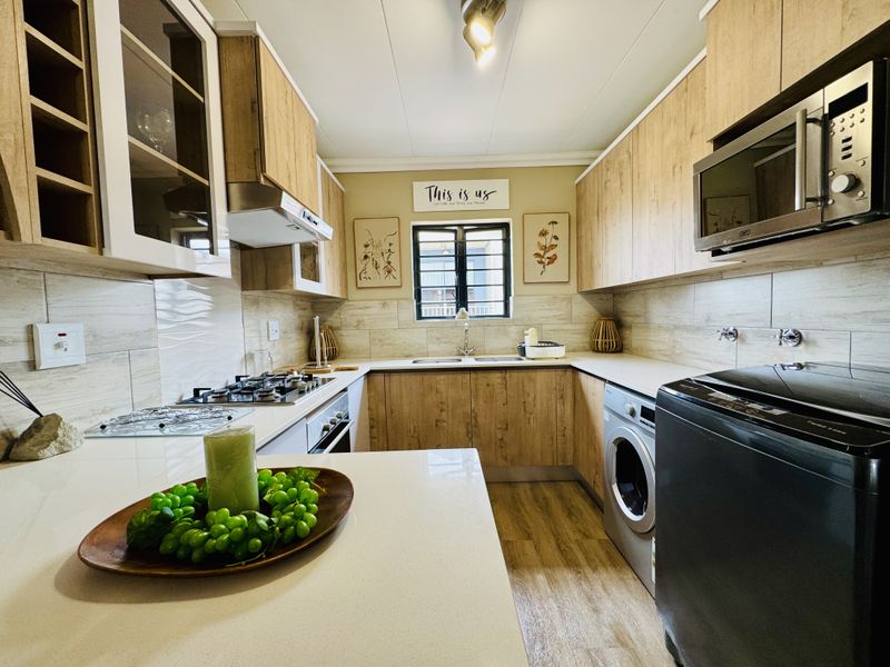Modern galley-style kitchen featuring wood-look cabinetry, stone countertops, integrated gas hob, built-in oven, extractor fan, and space for a front-loading washing machine.