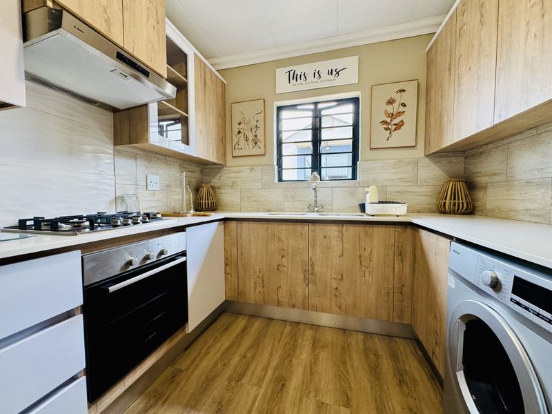 Modern kitchen featuring wood-look cabinetry, stone countertops, built-in oven, gas hob, extractor fan, and integrated space for a washing machine.