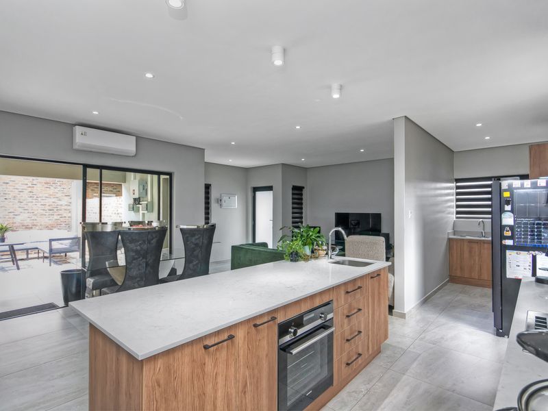 Modern open-plan living area featuring a contemporary kitchen with a central island, stone countertops, built-in oven, and seamless flow to the outdoor patio.