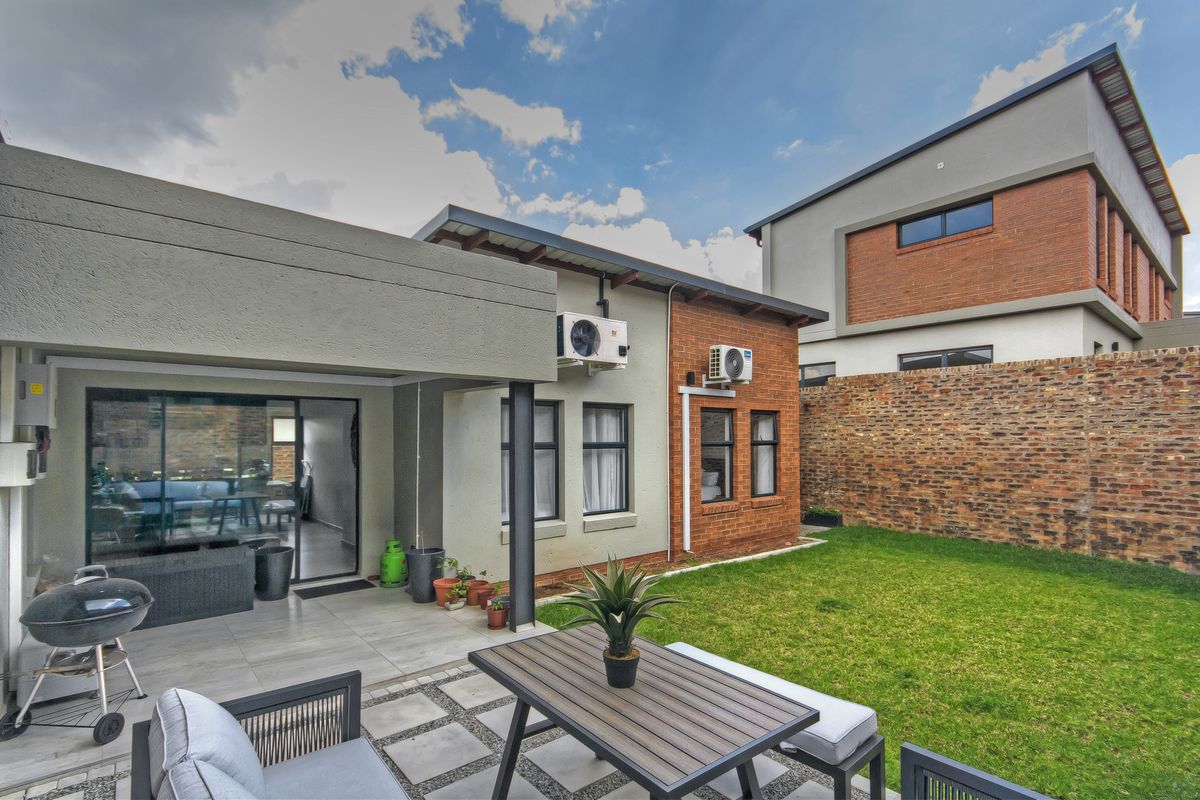 Rear view of the townhouse featuring a covered tiled patio, a private garden with lawn, and exterior brick and plaster finishes.