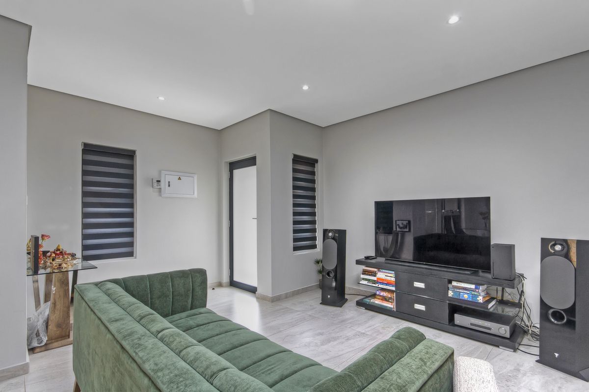 A modern living room featuring neutral walls, tiled flooring, recessed downlighting, and dual-tone roller blinds for privacy.