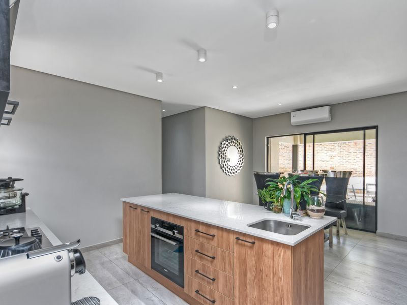 Modern open-plan kitchen featuring a central island with built-in oven, stone countertops, and seamless flow to the outdoor patio area.