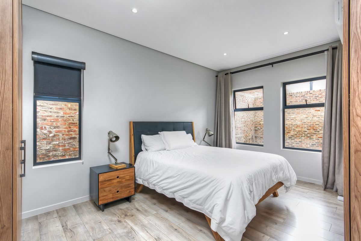 A modern, well-maintained bedroom featuring laminate flooring, recessed downlighting, built-in cupboards, and aluminium-framed windows with roller blinds.