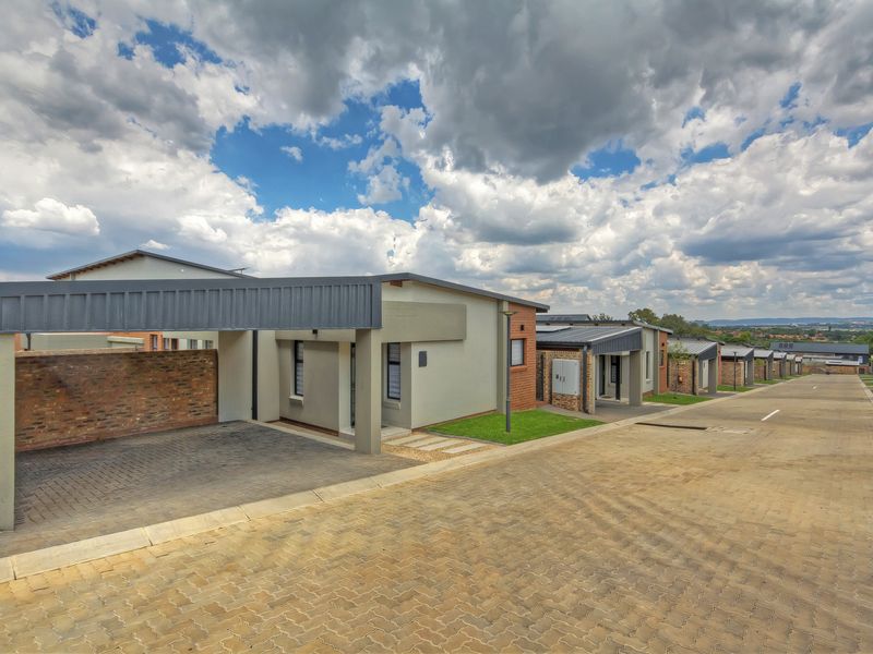 A street-level view of a modern townhouse complex featuring paved driveways, covered carports, and well-maintained brick and plastered exterior facades.