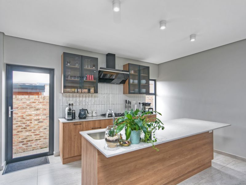 Modern kitchen featuring a central island with quartz countertops, wood-finish cabinetry, subway tile backsplash, and integrated extractor fan with direct access to the rear exterior.