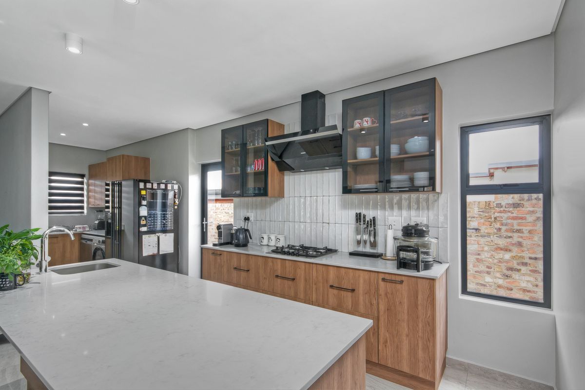 Modern kitchen featuring wood-grain cabinetry, quartz countertops, a central island, gas hob, and stylish subway tile backsplash with ample storage.