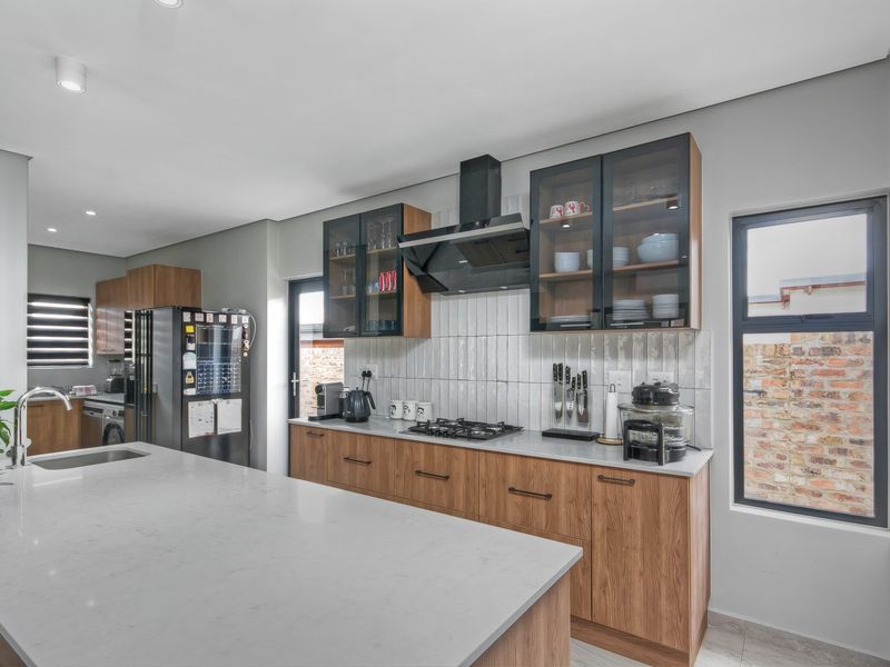 Modern kitchen featuring wood-grain cabinetry, quartz countertops, a central island, gas hob, and stylish subway tile backsplash with ample storage.