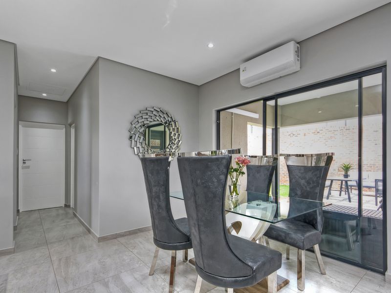 Modern dining area featuring neutral grey walls, large format floor tiles, recessed lighting, and sliding glass doors providing access to the outdoor patio.