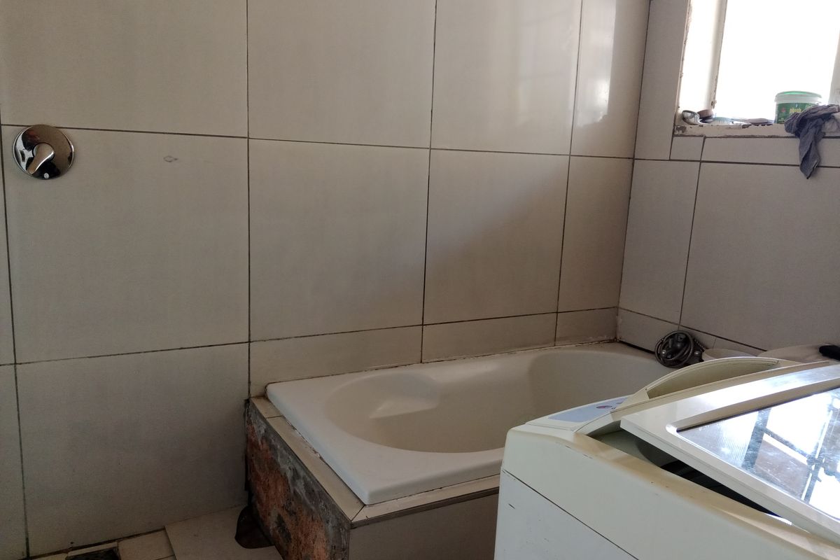 A bathroom featuring a built-in bathtub with tiled surround and wall-mounted mixer tap, requiring minor repairs to the bathtub apron and tiling.