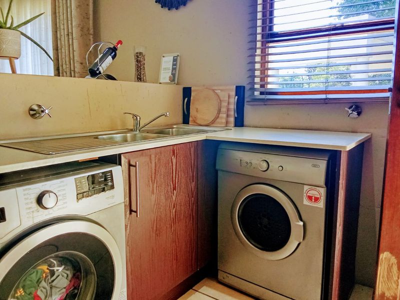 A functional laundry area featuring built-in wooden cabinetry, a stainless steel sink, and space for under-counter appliances.