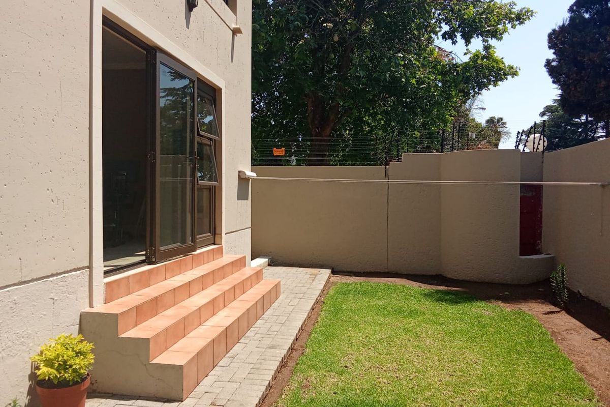 Rear exterior view featuring a small lawn, paved walkway, tiled steps leading to a sliding glass door, and a boundary wall with electric fencing.
