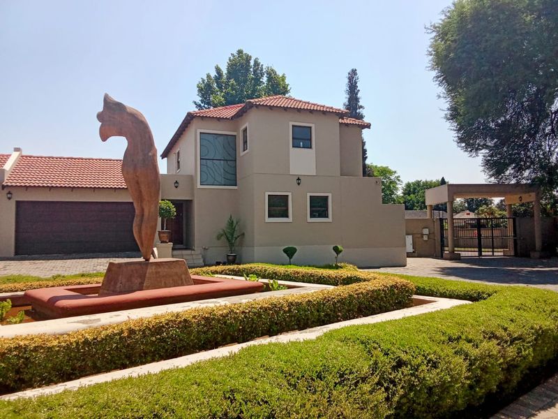 Front elevation of a double-story residence featuring a paved driveway, double garage, landscaped garden with a central water feature, and secure gated entrance.