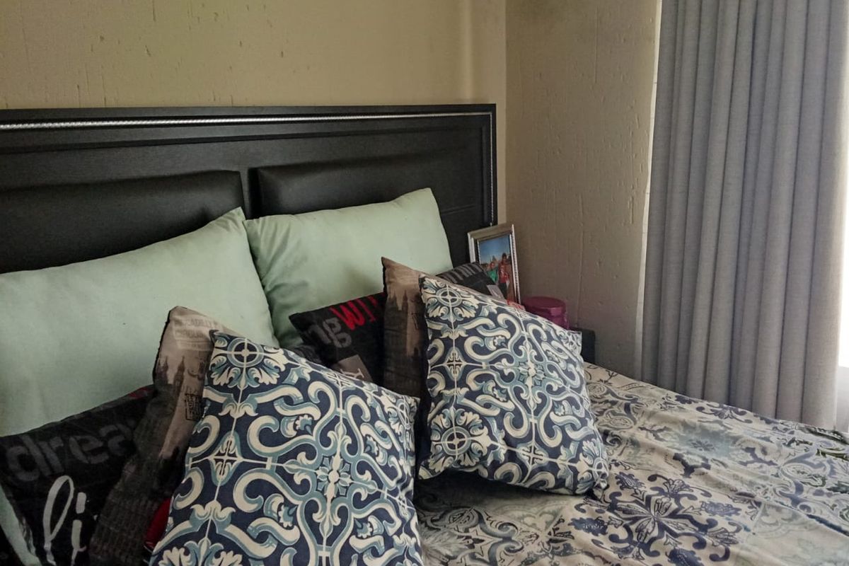 A bedroom featuring a dark headboard and window curtains, showing signs of wear on the wall surfaces.