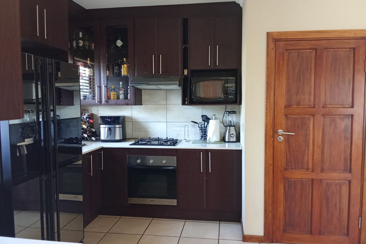 A functional kitchen featuring dark wood cabinetry, a gas hob, built-in oven, extractor fan, and tiled flooring, complemented by a solid wood door.