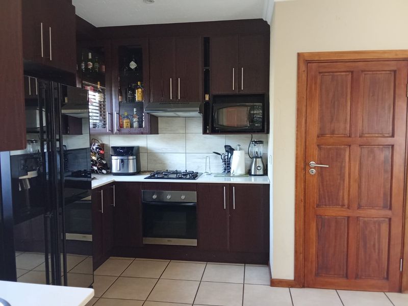 A functional kitchen featuring dark wood cabinetry, a gas hob, built-in oven, extractor fan, and tiled flooring, complemented by a solid wood door.