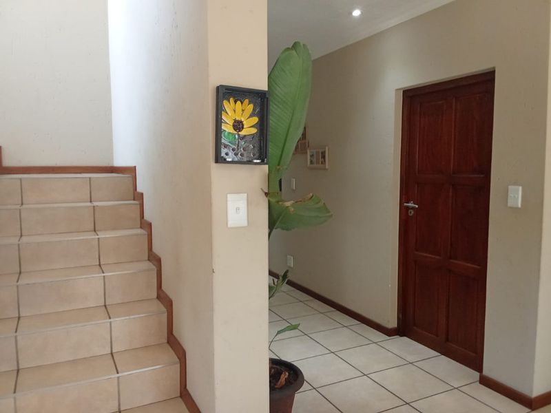 A bright hallway featuring tiled flooring and a staircase with a wooden handrail, leading to a solid wood door.