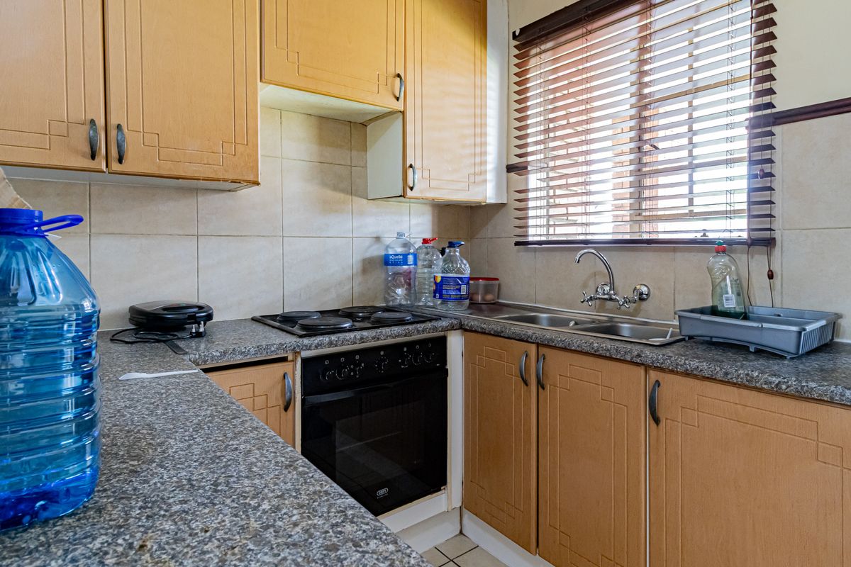 Compact kitchen featuring light wood cabinetry, granite-look countertops, a built-in oven with electric hob, and a double stainless steel sink.