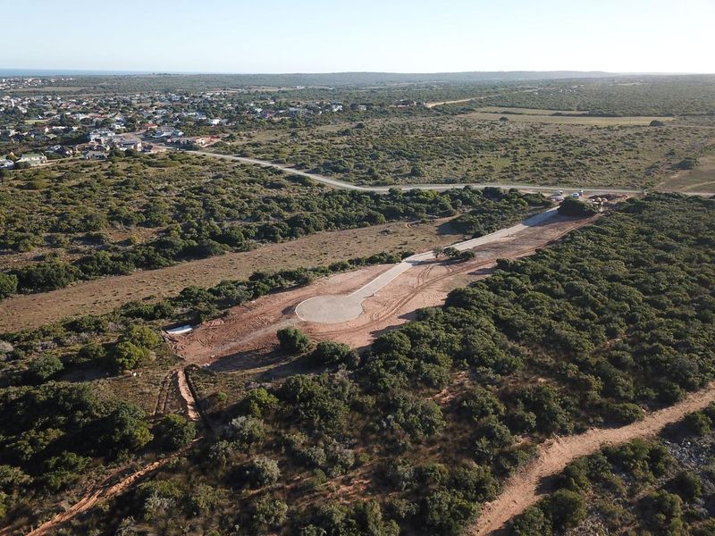 Aerial view of a vacant residential plot featuring a newly paved cul-de-sac and access road, situated within a natural coastal landscape.