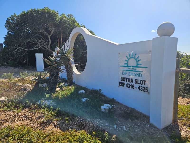 A well-maintained entrance wall and signage for the Die Eiland estate, featuring a modern architectural design and landscaped garden area.