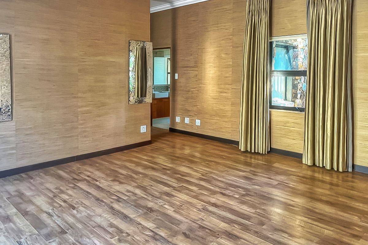 Spacious bedroom featuring wood-look laminate flooring and textured wall paneling, with an adjoining bathroom visible through the doorway.