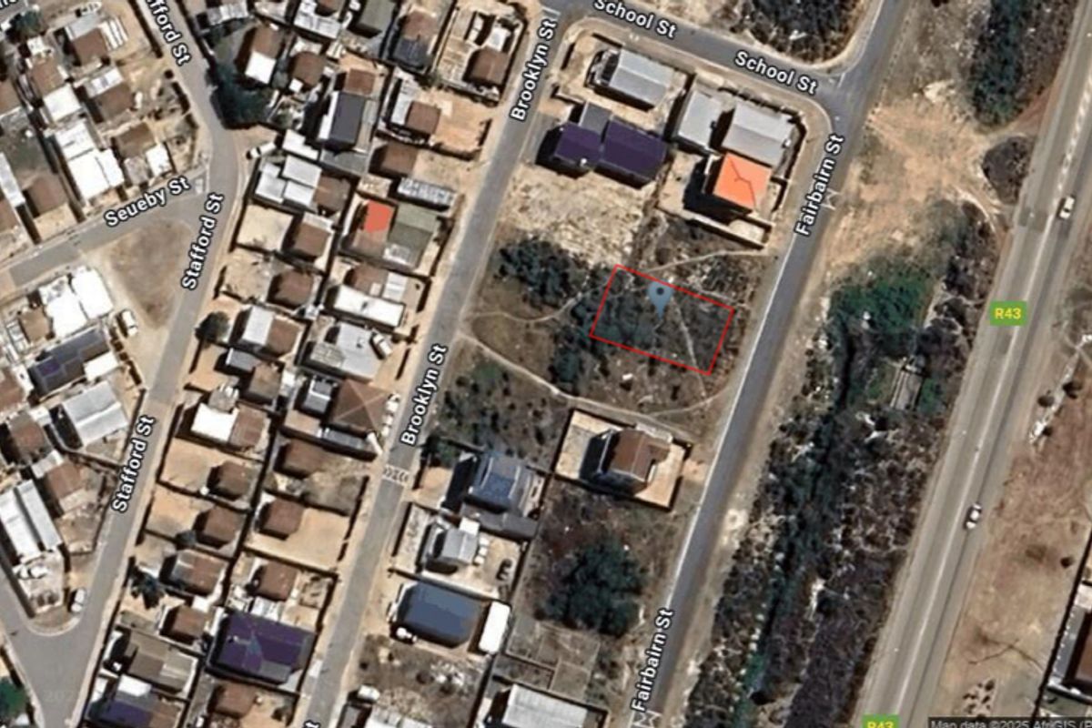 Aerial view of a vacant residential plot highlighted in red, situated in a developed neighborhood near main roads.