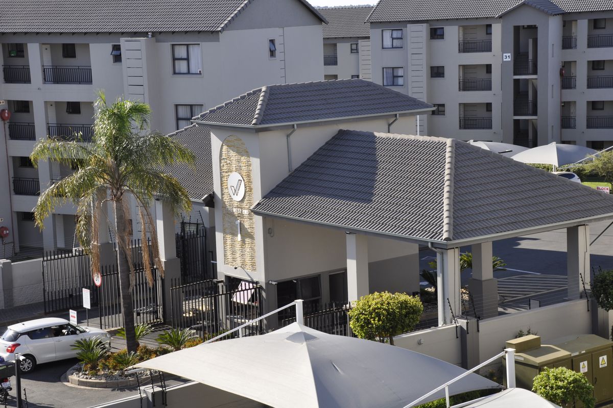Aerial view of the apartment complex entrance featuring a security gatehouse, tiled roofing, and landscaped grounds.