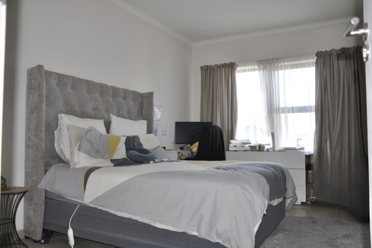 A bedroom featuring neutral wall tones, tiled flooring, and a large window with curtain treatments, providing natural light to the space.