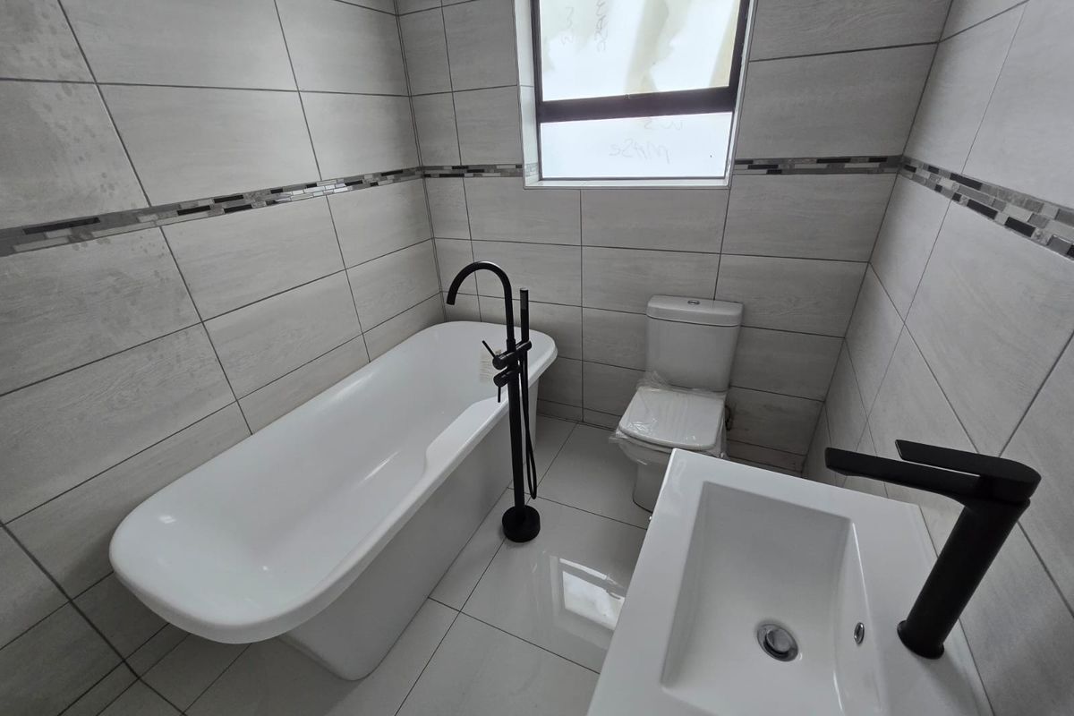 Modern bathroom featuring a sleek freestanding bathtub, matte black fixtures, and contemporary neutral wall and floor tiling.