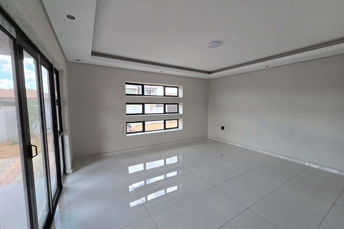 A bright, modern, and empty living area featuring polished tiled floors, recessed ceiling details, and large sliding glass doors leading to the exterior.