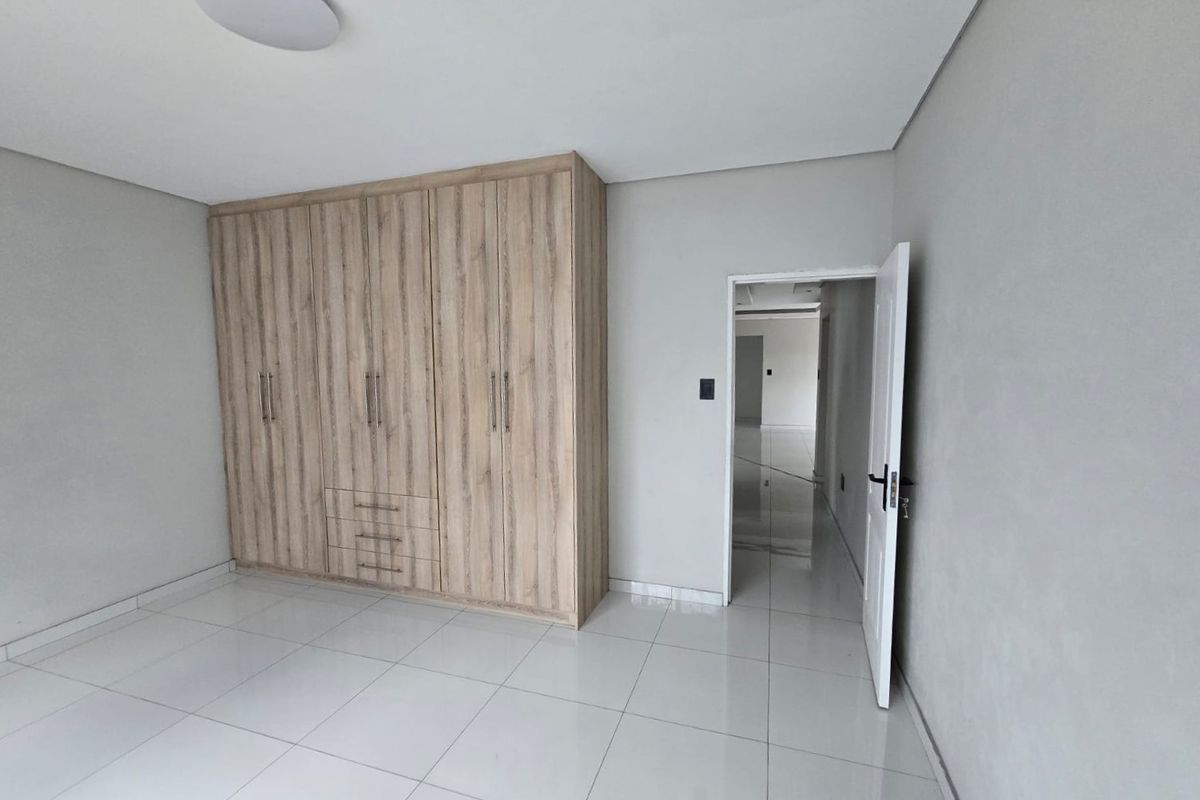A clean, empty bedroom featuring light wood-finish built-in wardrobes, neutral grey walls, and polished white floor tiles.