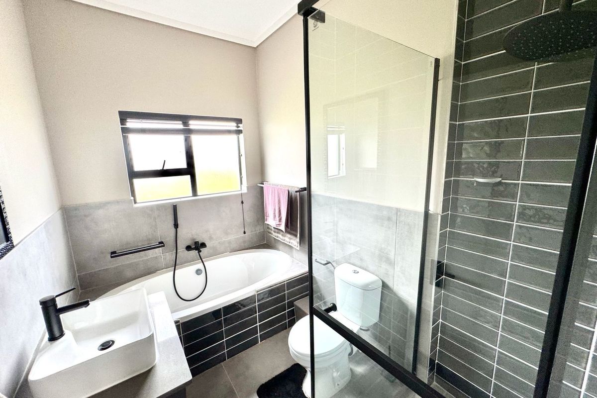Modern bathroom featuring a glass-enclosed shower, a built-in bathtub, a contemporary vanity basin, and stylish dark grey tiling.
