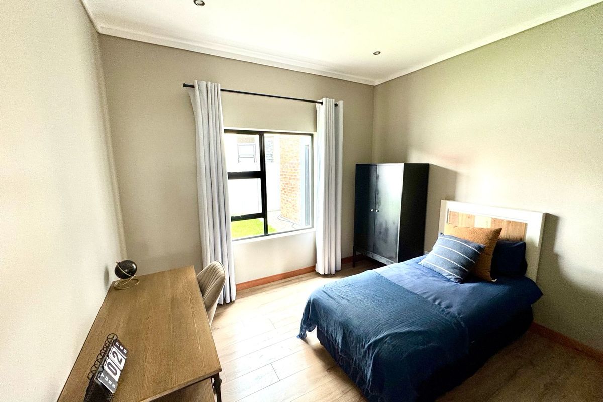 A well-maintained bedroom featuring neutral wall tones, wood-look flooring, recessed ceiling lighting, and a large window providing natural light.