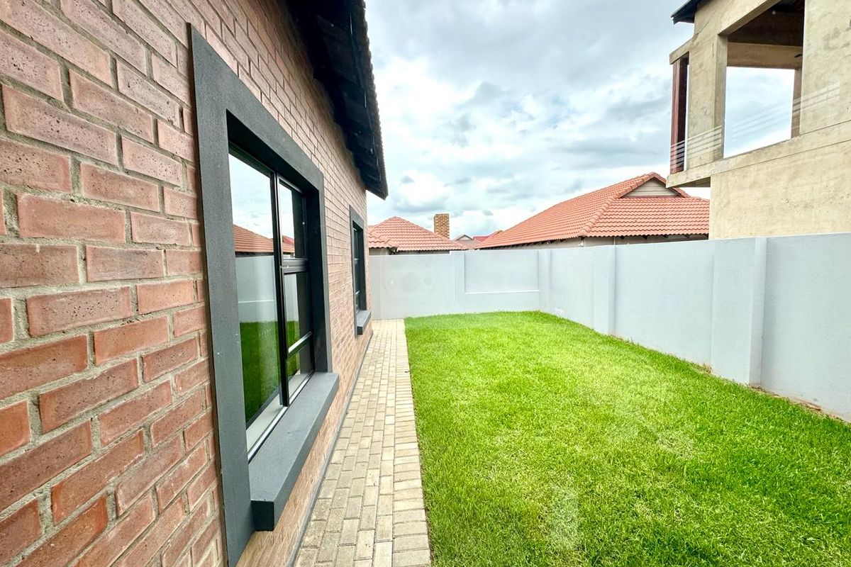 A well-maintained rear garden featuring a brick-paved walkway, manicured lawn, and perimeter boundary wall, providing a clean and private outdoor space.
