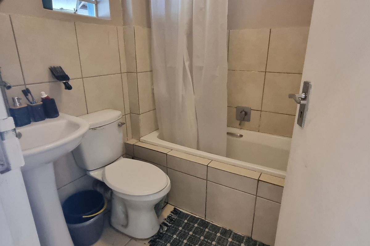 A compact bathroom featuring a pedestal basin, toilet, and a bathtub with a shower curtain, finished with neutral wall tiling.
