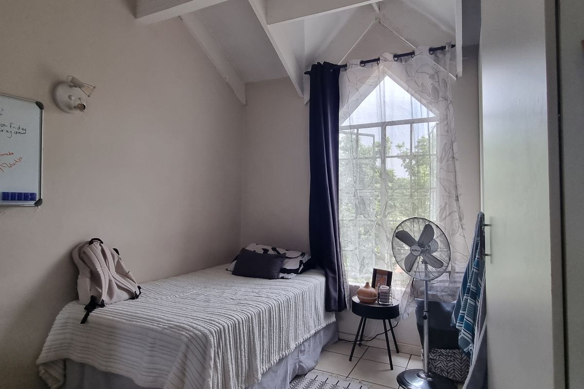A cozy bedroom featuring a vaulted ceiling, tiled flooring, and a distinctive gabled window, providing a bright and functional living space.