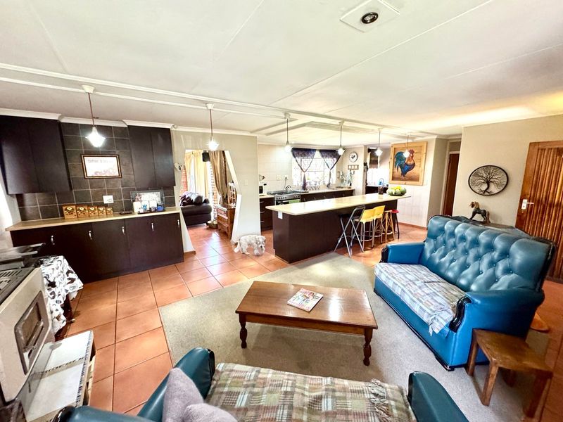 Spacious open-plan living area featuring a functional kitchen with a breakfast island, tiled flooring, and integrated cabinetry, seamlessly connecting to the lounge space.