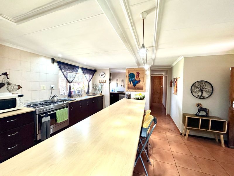 Spacious kitchen featuring dark cabinetry, a large breakfast bar, gas stove, and tiled flooring, offering a functional layout with direct access to the hallway.