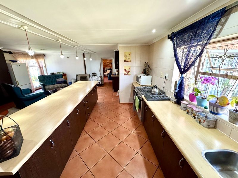 Open-plan kitchen featuring a long central island, dark cabinetry, gas hob, and tiled flooring, flowing into the adjacent living area.