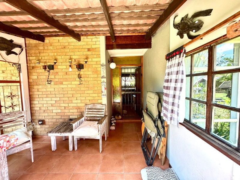 Covered patio area featuring exposed brickwork, timber beam ceiling, and tiled flooring, providing a rustic outdoor space with direct access to the home.