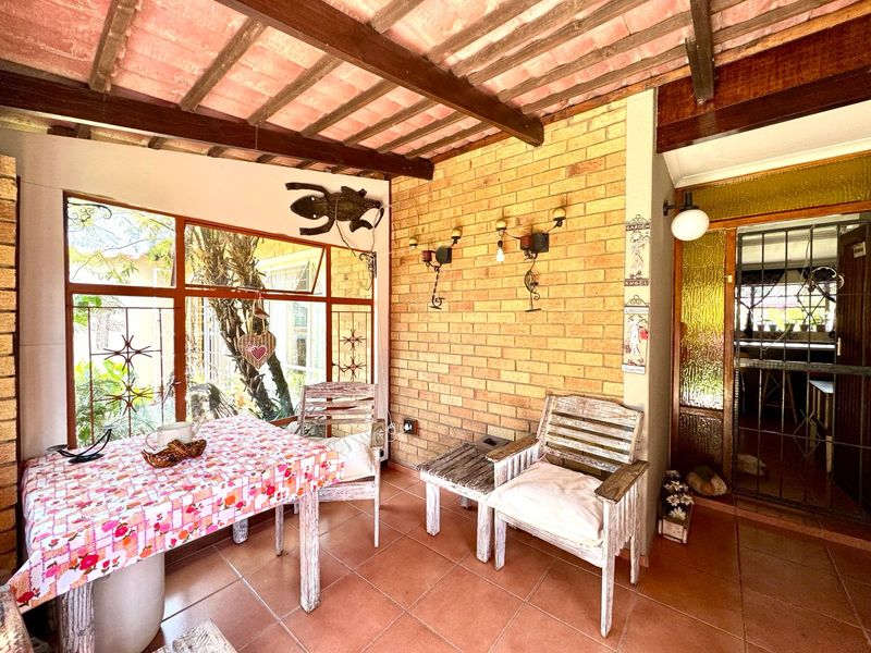 A covered patio area featuring exposed brick walls, timber beam ceilings, and large windows, providing a rustic outdoor living space.