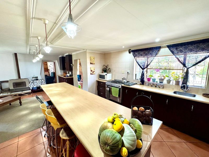 Spacious open-plan kitchen featuring a large island, dark cabinetry, stainless steel stove, and tiled flooring, seamlessly flowing into the adjacent living area.