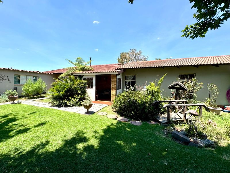 A view of the rear exterior of the house featuring a tiled roof, covered patio area, and a well-maintained garden with paved pathways.
