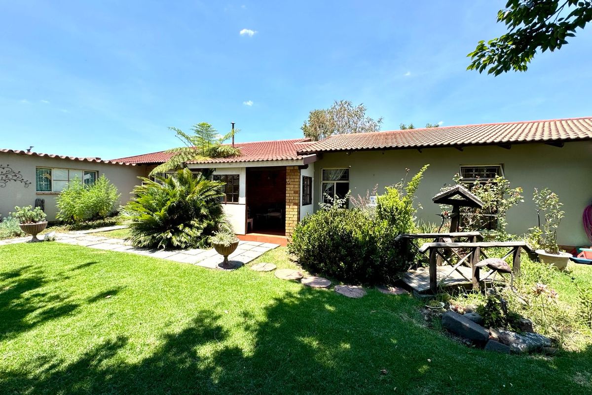 A view of the rear exterior of the house featuring a tiled roof, covered patio area, and a well-maintained garden with paved pathways.
