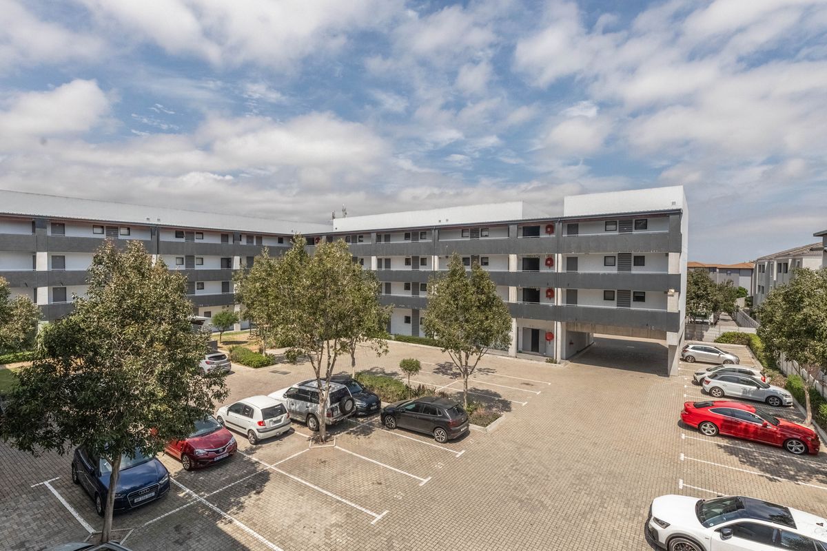 An elevated view of the apartment complex courtyard featuring paved parking bays, landscaped trees, and multi-story residential building facades.