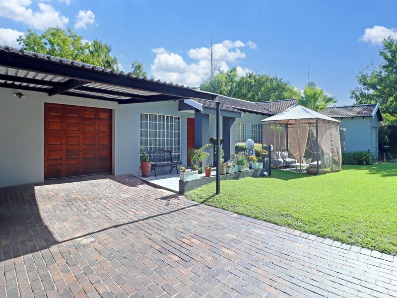 Front exterior view of the house featuring a brick driveway, covered carport, garage access, and a well-maintained front lawn.