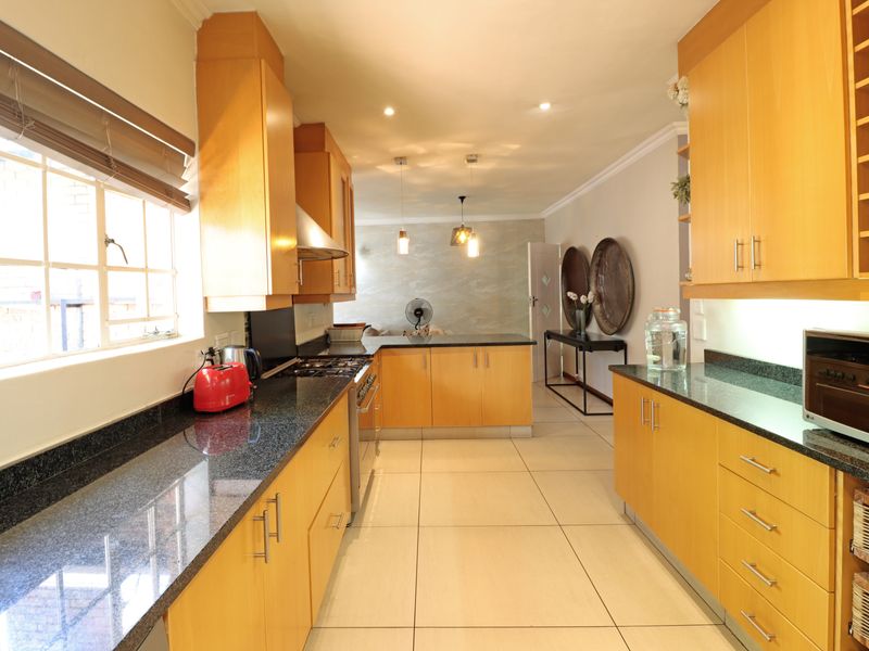 A well-maintained kitchen featuring wooden cabinetry, granite countertops, a gas hob, and an integrated oven, with tiled flooring throughout.