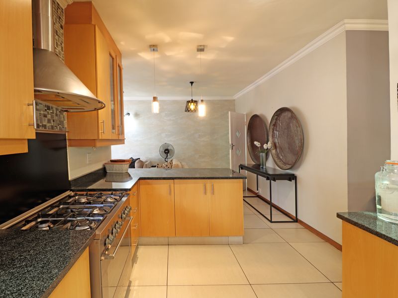 Open-plan kitchen featuring light wood cabinetry, granite countertops, gas hob, and extractor fan, flowing into a connected living area with tiled flooring.