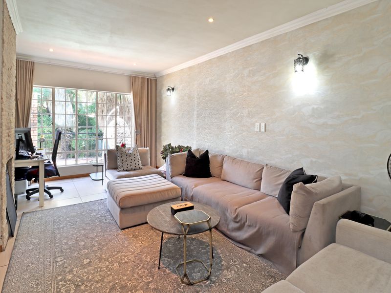 A well-lit living room featuring a textured feature wall, tiled flooring, recessed downlighting, and large windows providing natural light.