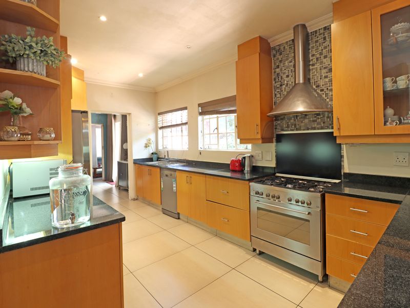 A well-maintained kitchen featuring wooden cabinetry, granite countertops, a stainless steel gas stove with extractor fan, and a decorative mosaic tile backsplash.