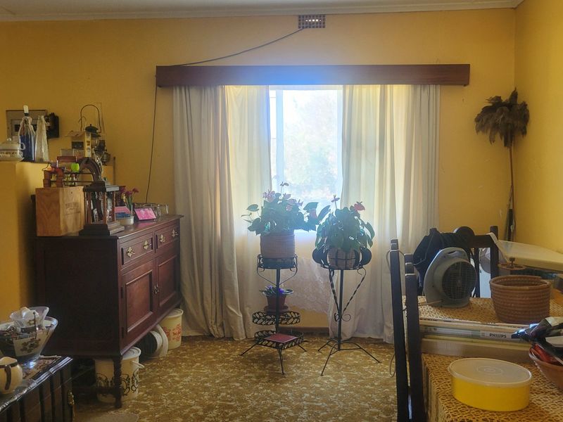 A living area featuring yellow walls, a window with curtains, and patterned carpet flooring, offering potential for modernization and aesthetic updates.